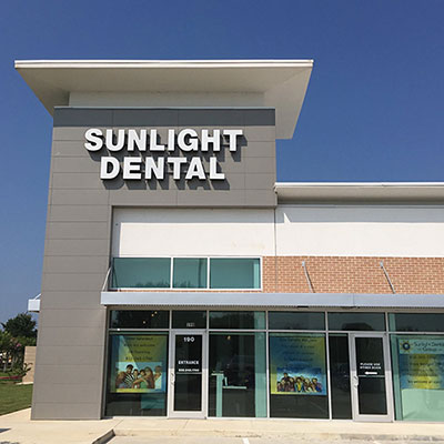 The image shows a sign for Sunlight Dental in front of a building with a clear sky and no visible people.